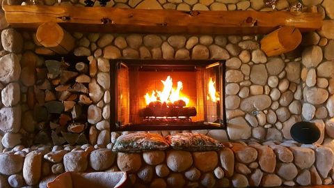 Electric fireplace with a stone mantel and cabin log shelf.
